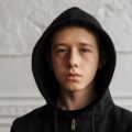 Teenager in black hoodie sitting indoors, contemplating with a serious expression. managing anger for teens