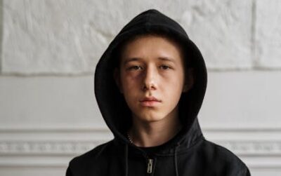 Teenager in black hoodie sitting indoors, contemplating with a serious expression. managing anger for teens