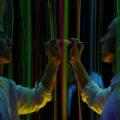 A man interacts with mirrored neon threads, creating vibrant reflections in a dark setting.