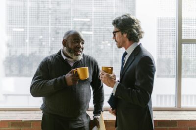 Two senior businessmen in conversation, enjoying coffee in a bright office space.Communication Skills